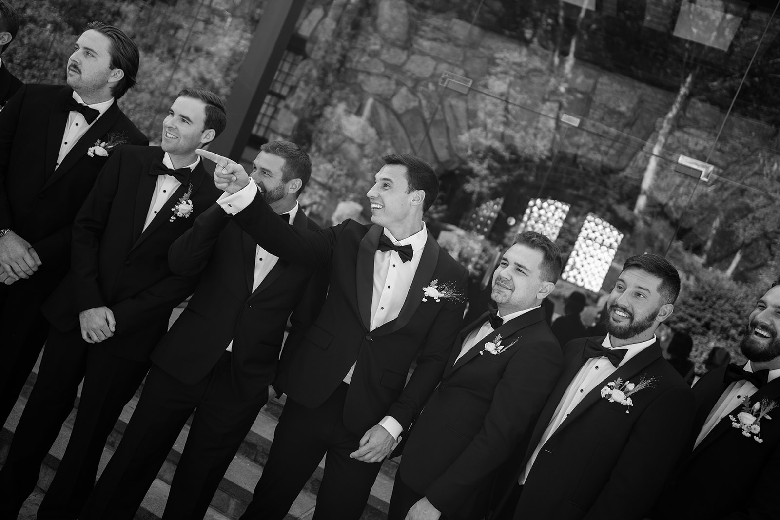 Black and white film photo of the groom and groomsmen sharing a candid laugh while looking off-camera.